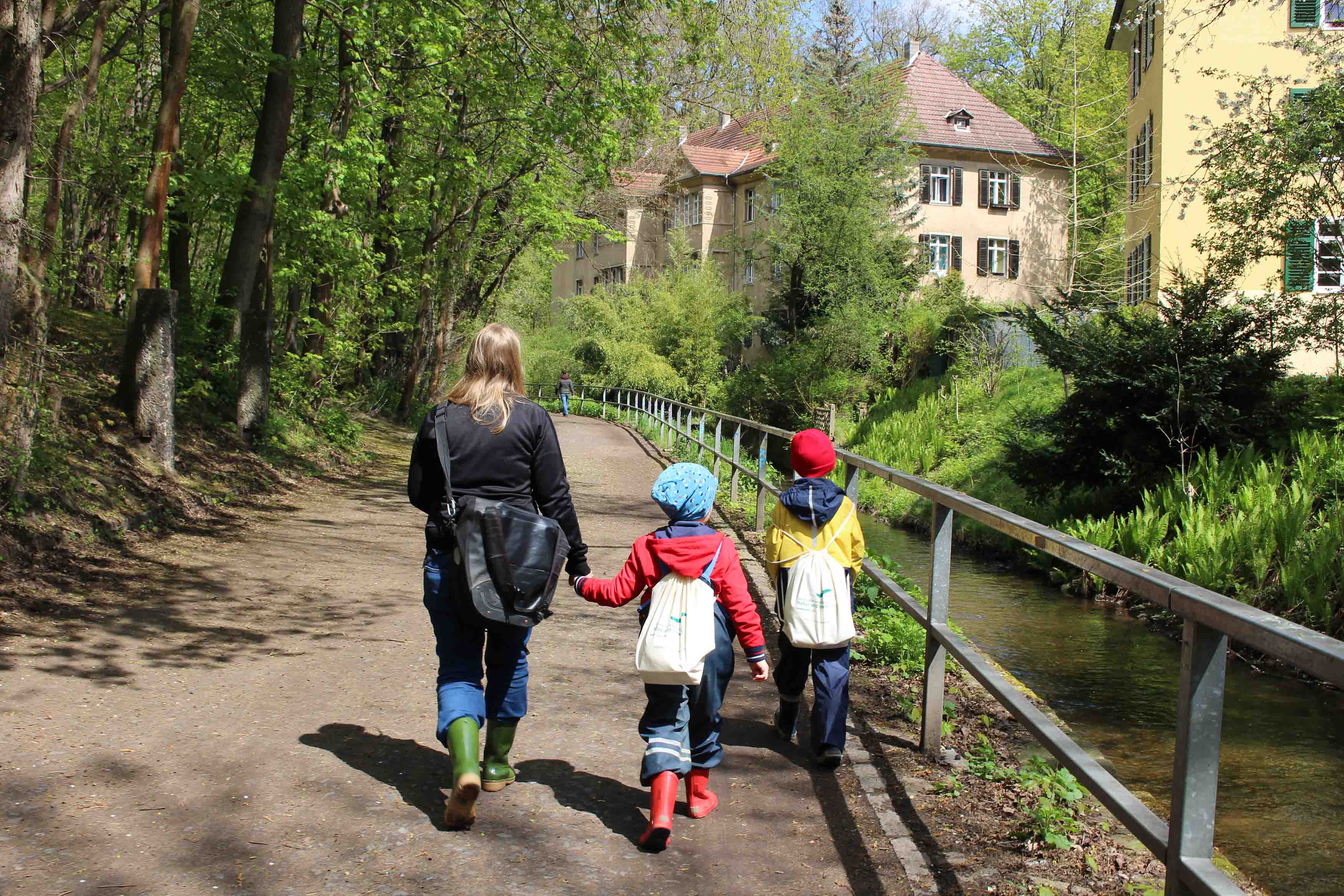 Familie beim Spaziergang entlang der Prießnitz, die Kinder tragen Gummistiefel und Entdecker-Rucksäcke.