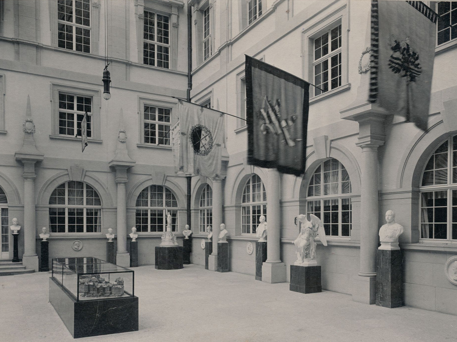 KI generiert: Das Bild zeigt den Innenhof eines Museums in Dresden im Jahr 1911. Im Vordergrund sind mehrere Statuen und Vitrinen sowie hängende Flaggen zu sehen.