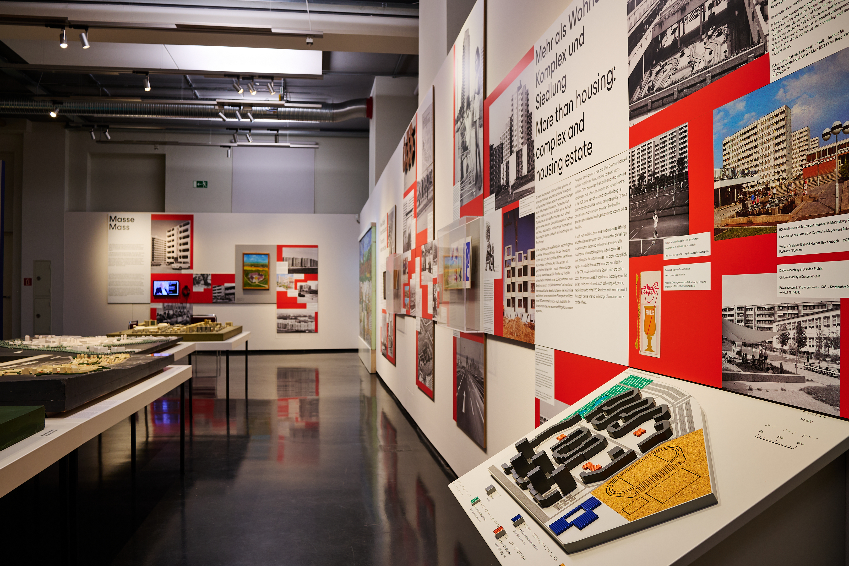 AI generated: The picture shows an exhibition in a museum that deals with architecture and residential complexes. There are various models, photos and information boards illustrating the topic.