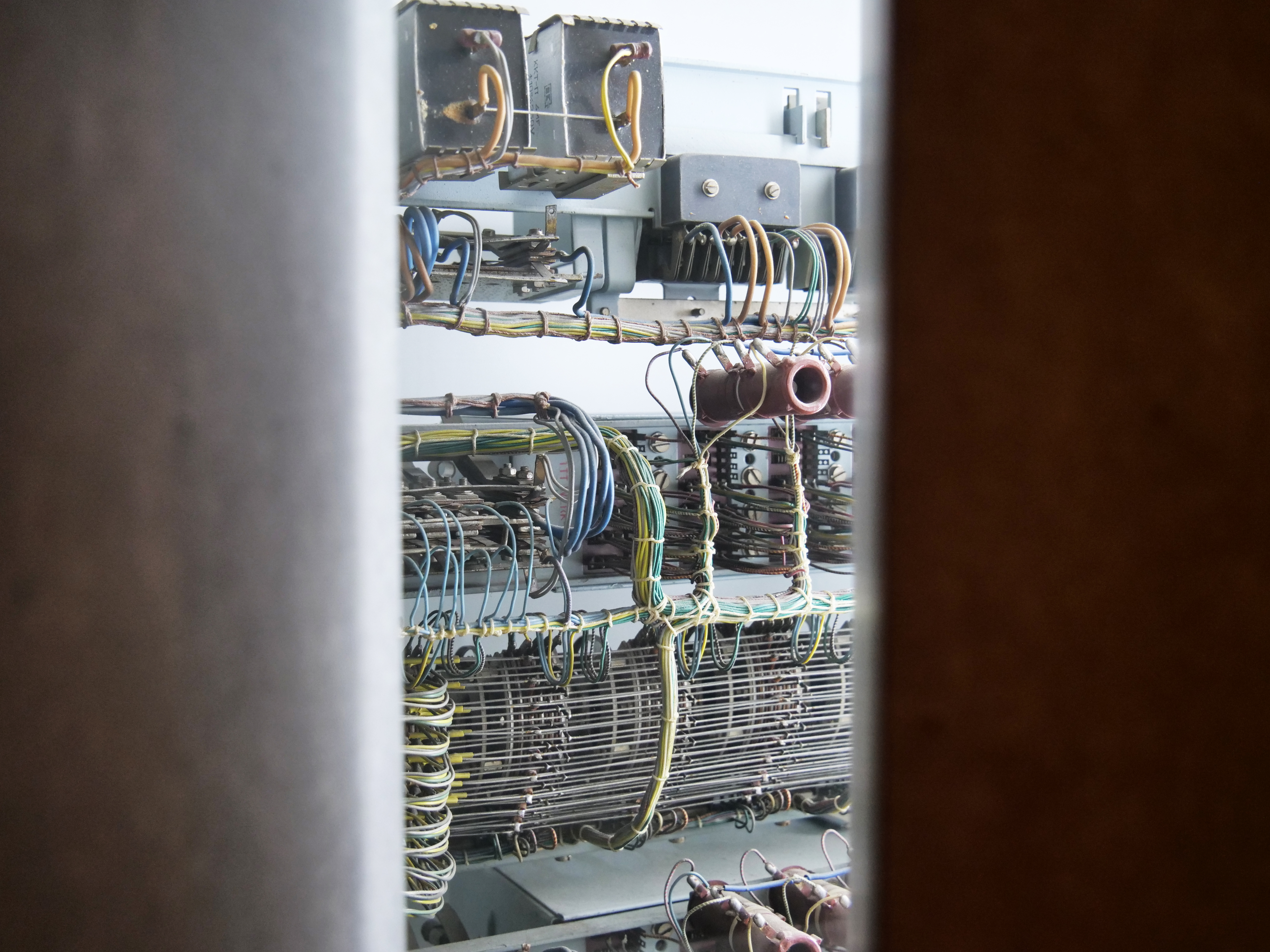 KI generiert: Das Bild zeigt die interne Verkabelung eines alten elektrischen oder elektronischen Geräts mit Reihen von Drähten und Komponenten. Diese sind in einem Gehäuse oder Raum eingeschlossen und erscheinen durch einen schmalen Spalt betrachtet.