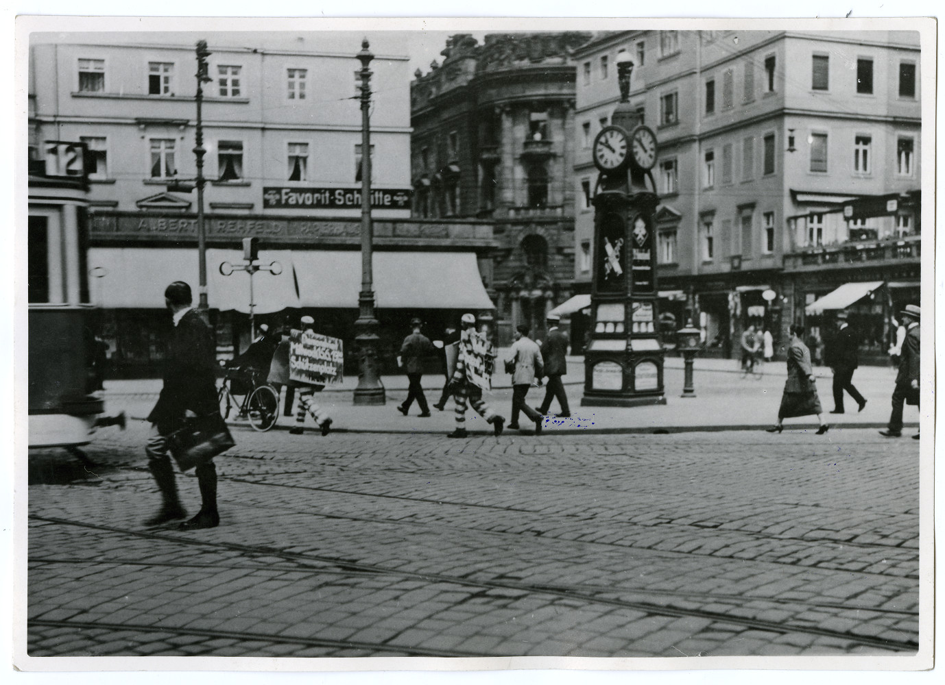 KI generiert: Das Bild zeigt eine belebte Straßenszene in einer Stadt, mit Passanten, einem stilvollen Uhrturm und mehreren Gebäuden im Hintergrund. Im Vordergrund befindet sich ein Mann im Anzug, der eine Tasche trägt und die Straße überquert.