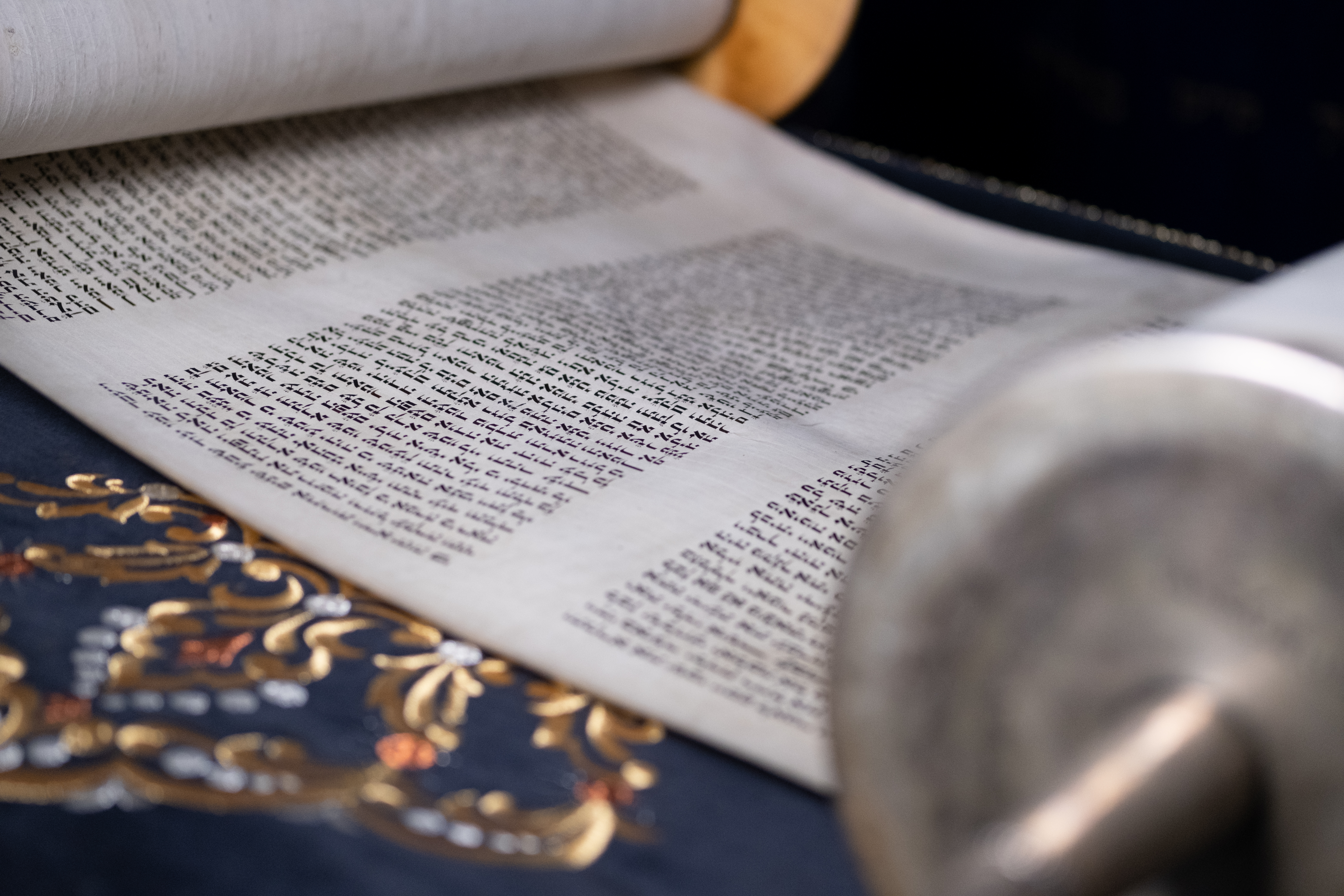 KI generiert: Das Bild zeigt eine aufgerollte Schriftrolle mit hebräischem Text auf einem verzierten Untergrund. Der Hauptinhalt ist die Schriftrolle und der elegante Hintergrund.