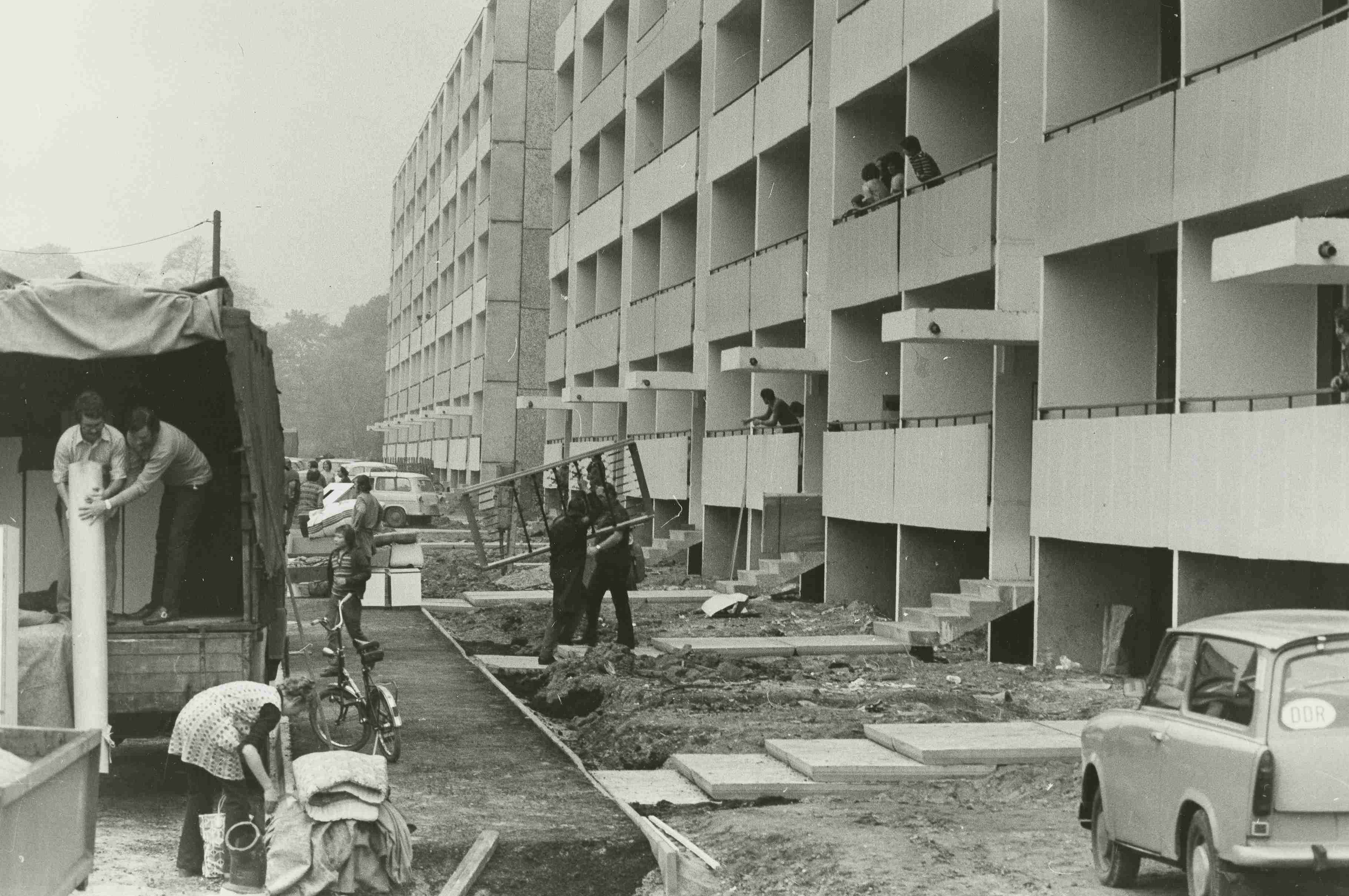 KI generiert: Das Bild zeigt eine Gruppe von Kindern, die auf einem Spielplatz spielen und durch eine bunt bemalte Mauer mit Kreisen krabbeln und klettern. Im Hintergrund sind große Wohngebäude zu sehen.
