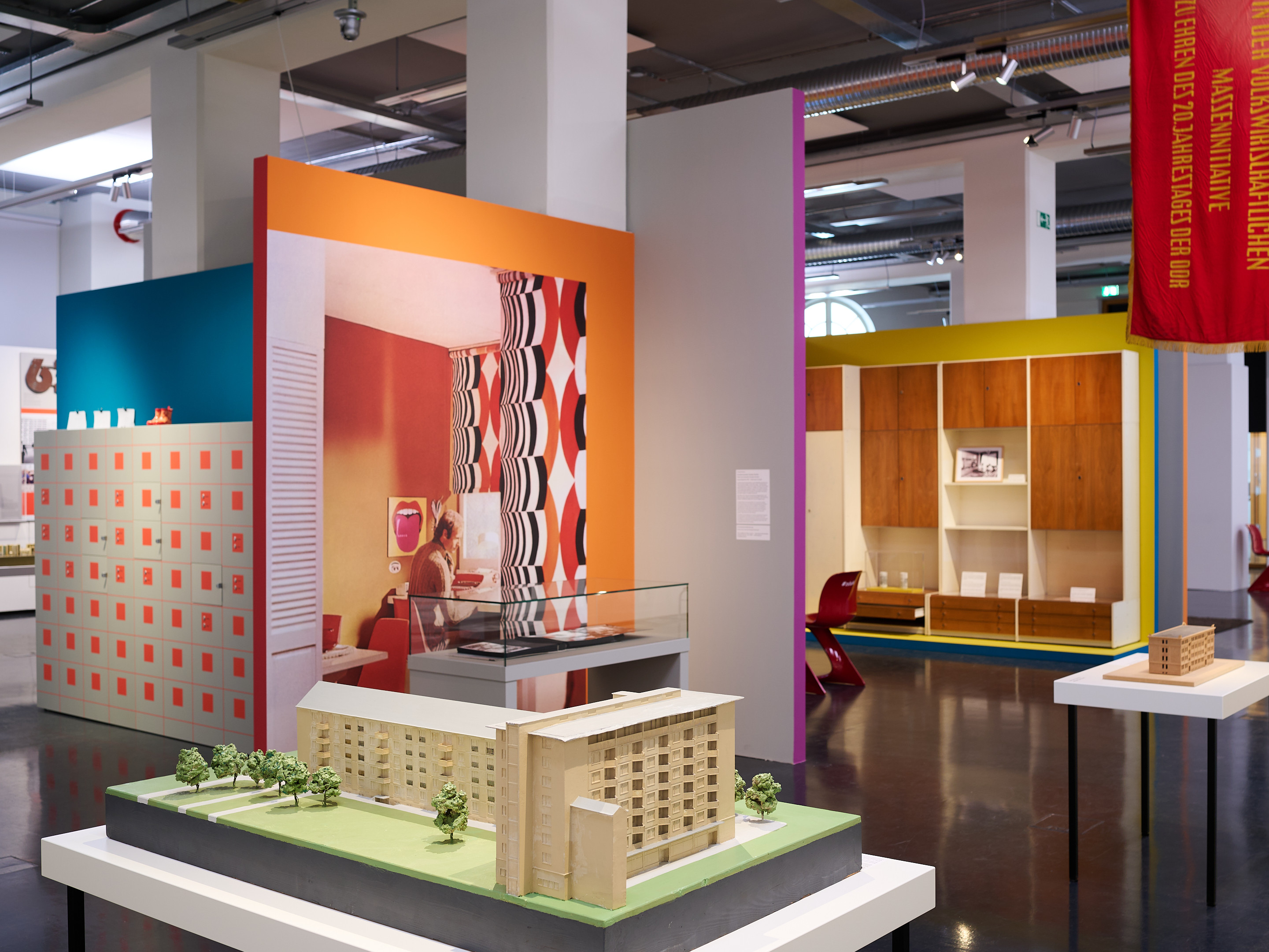 KI generated: The image shows a colourful information board with the heading "PLATTE OST WEST", which deals with large panel construction in housing. There are explanatory texts in German and English about this construction concept.