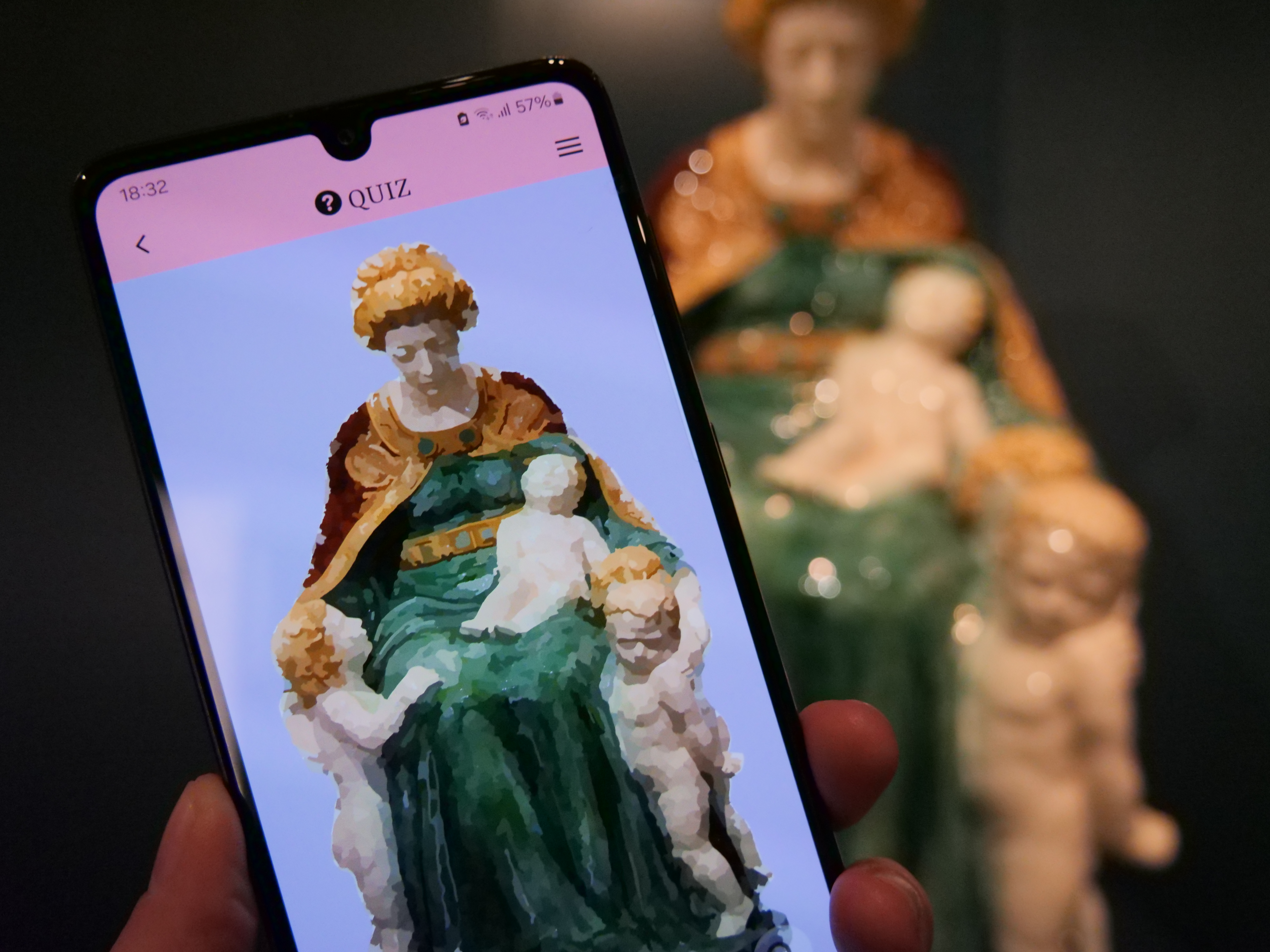 KI generiert: Das Bild zeigt eine Person, die eine Smartphone-App verwendet, um ein Foto einer Skulptur zu identifizieren. Im Hintergrund sieht man die tatsächliche Skulptur, die auf dem Handybildschirm in einer digital bearbeiteten Version dargestellt ist.
