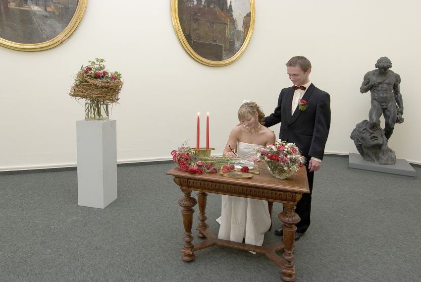 Ein junges Brautpaar im Festsaal, die Braut unterschreibt gerade die Eheurkunde.
